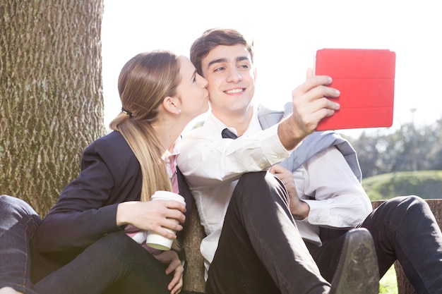 Muchacha que sostiene un café y besando la mejilla de su novio