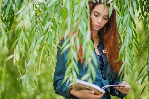 Muchacha que sostiene los cuadernos que leen en parque