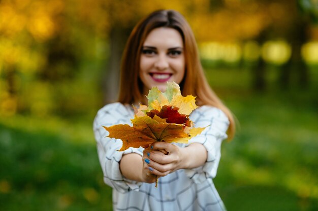 Muchacha que sostiene las hojas de otoño en ambas manos en el parque.