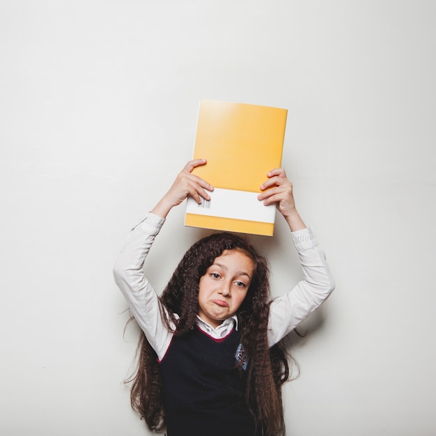 Muchacha que sostiene el libro de ejercicio sobre la cabeza