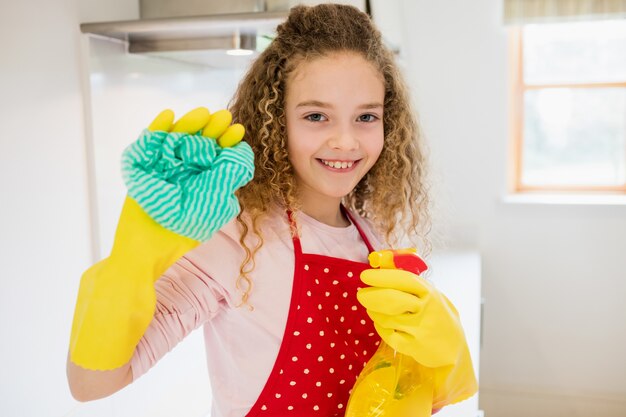 Muchacha que sostiene la servilleta y botella de spray en la cocina