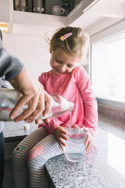 Foto gratuita muchacha que sostiene el vidrio mientras que su padre que vierte el agua en cocina