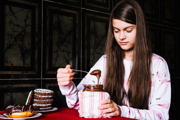 Foto gratuita muchacha que toma el chocolate derretido con la cuchara del tarro en la tabla