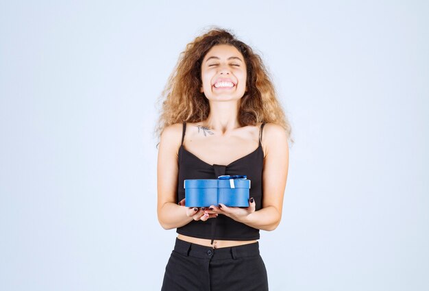 Muchacha rubia que sostiene una caja de regalo azul y parece sorprendida.