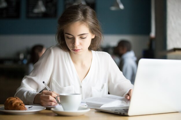 Muchacha seria que estudia en el café que hace las notas que se preparan para el examen