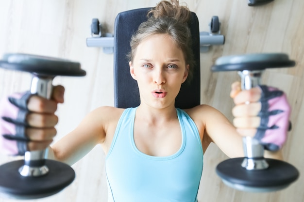 Muchacha seria que miente y que levanta dos pesas de gimnasia