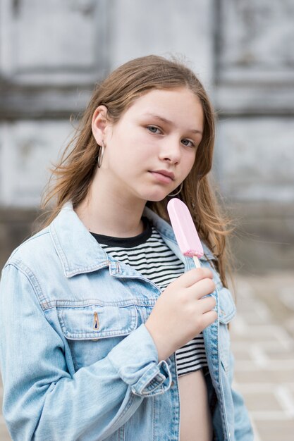 Muchacha seria que sostiene el helado rosado que mira la cámara