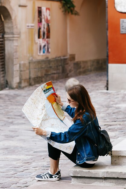 La muchacha se sienta en los pasos mira el mapa turístico