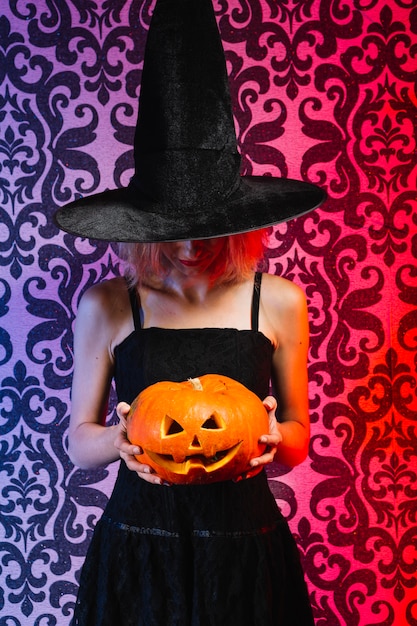 Muchacha en sombrero de la bruja que sostiene la calabaza