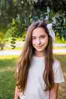 Foto gratuita muchacha sonriente adorable que se coloca delante de un árbol en parque