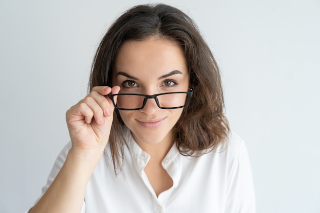 Muchacha sonriente alegre que quita los vidrios. Mujer caucásica joven que mira a escondidas sobre las lentes.