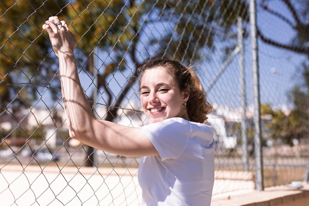 Foto gratuita muchacha sonriente joven que se sostiene sobre la cerca del metal