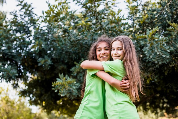 Muchacha sonriente que se abraza contra árbol verde