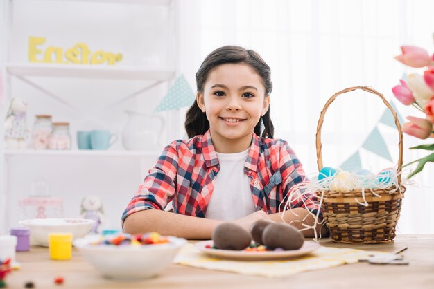 Muchacha sonriente que se coloca detrás de la tabla con los huevos de Pascua del chocolate