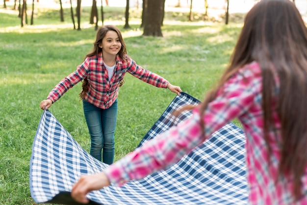 Muchacha sonriente que coloca la manta en hierba con su madre