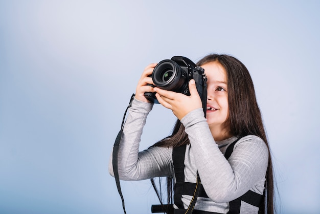 Muchacha sonriente que fotografía a través de cámara contra cámara azul