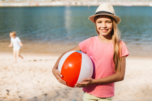 Muchacha sonriente que lleva la pelota de playa ambas manos