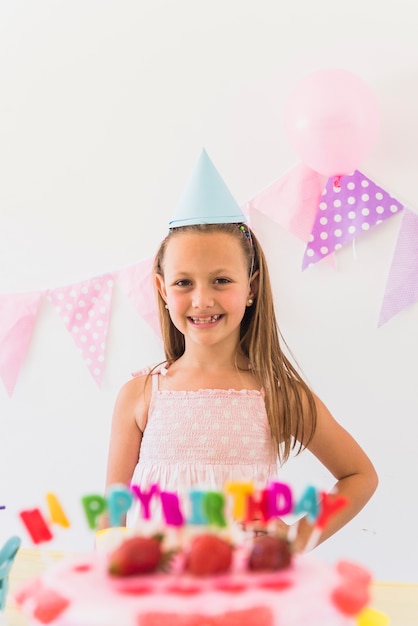 Muchacha sonriente que presenta detrás de la torta de cumpleaños en partido