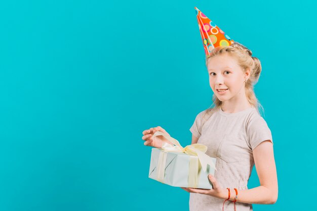 Muchacha sonriente que sostiene el regalo de cumpleaños en fondo coloreado turquesa