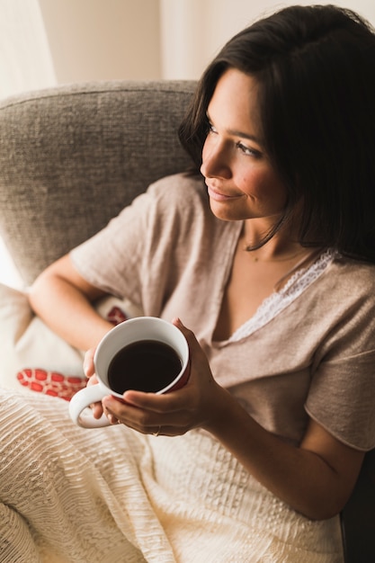 Muchacha sonriente que sostiene la taza de café en manos