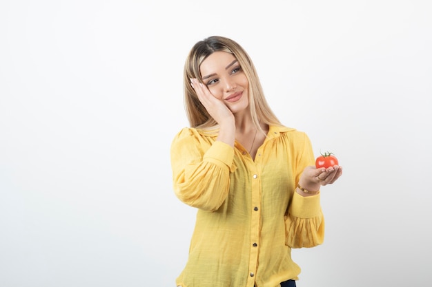 Muchacha sonriente que sostiene el tomate rojo y que presenta en blanco.