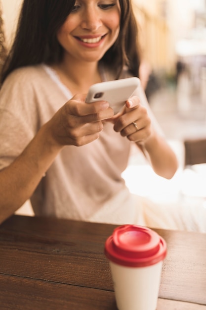 Muchacha sonriente que toma la imagen de la taza disponible a través del teléfono celular