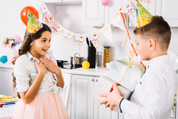 Muchacha sorprendida del cumpleaños que mira al muchacho que lleva las cajas de regalo en la mano