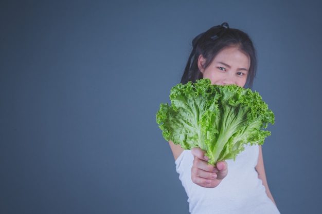 La muchacha sostiene las verduras en un fondo gris.