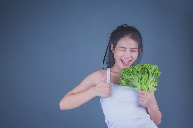 La muchacha sostiene las verduras en un fondo gris.