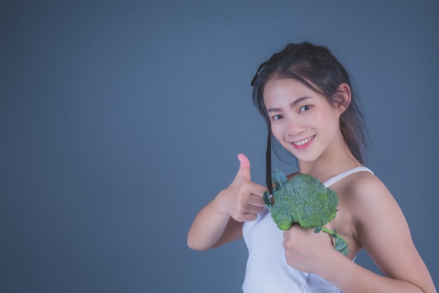 La muchacha sostiene las verduras en un fondo gris.