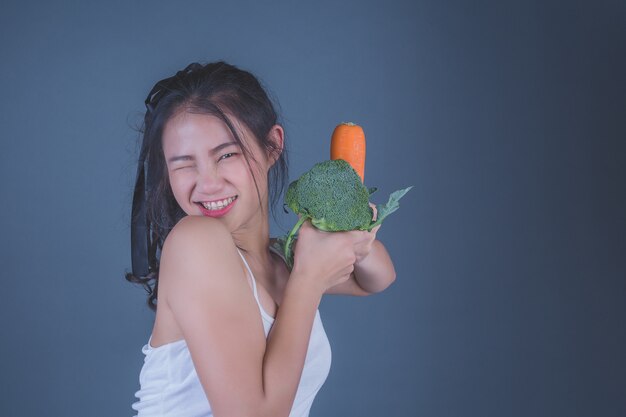 La muchacha sostiene las verduras en un fondo gris.