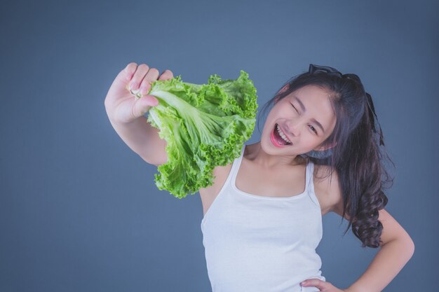 La muchacha sostiene las verduras en un fondo gris.