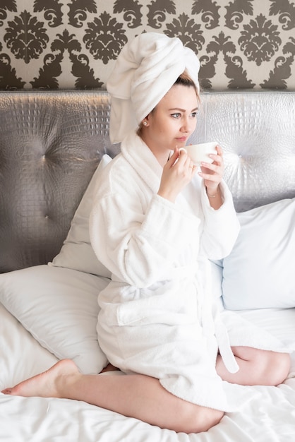 Foto gratuita muchacha con la taza de café en la cama que mira lejos