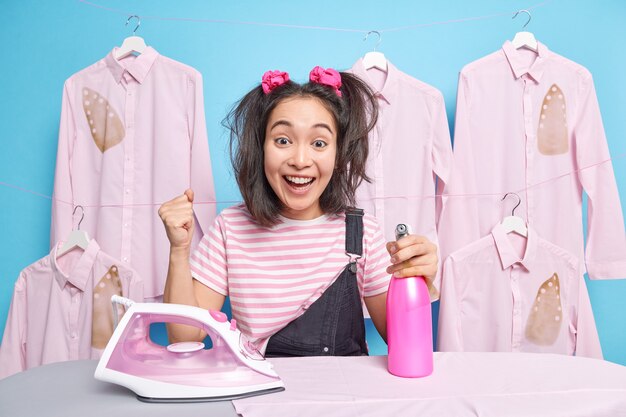 La muchacha trabajadora ocupada aprieta el puño y celebra terminar las tareas del hogar contra las camisas planchadas quemadas.