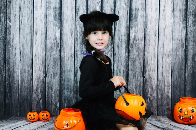 Muchacha en traje del gato que sostiene la cesta de la jack-o-linterna