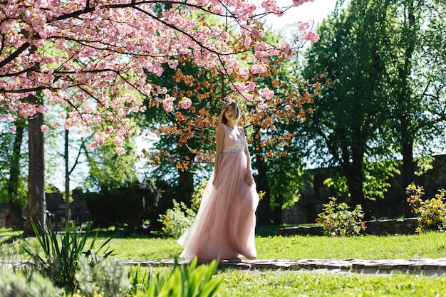 Foto gratuita la muchacha en vestido rosado se coloca bajo árbol floreciente de sakura en el parque