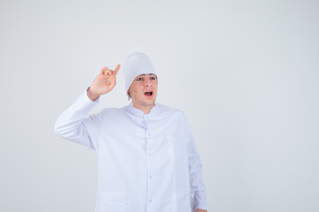 muchacho adolescente apuntando hacia arriba en uniforme de médico y mirando perplejo