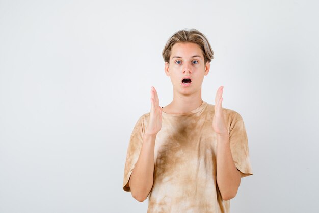 Muchacho adolescente en camiseta mostrando signo de tamaño y mirando sorprendido, vista frontal.