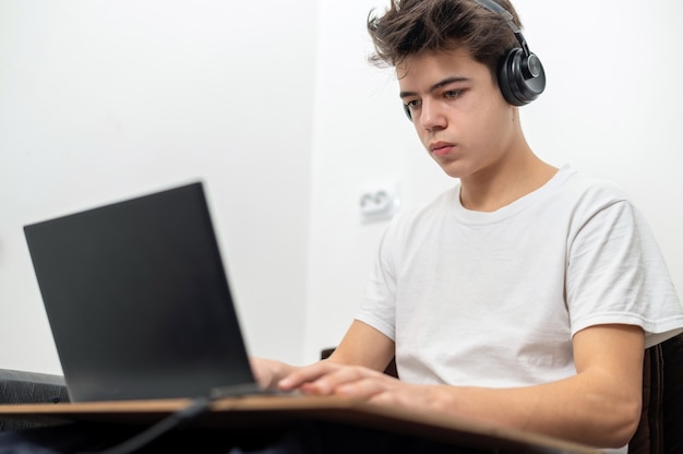 El muchacho adolescente está usando la computadora portátil con los auriculares en casa. Rostro serio y concentrado