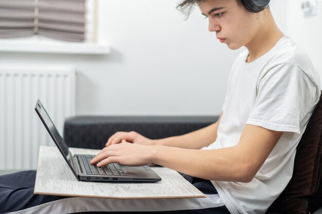 El muchacho adolescente está usando la computadora portátil con los auriculares en casa. Rostro serio y concentrado