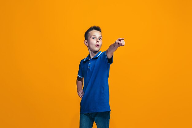 El muchacho adolescente feliz apuntando a ti, retrato de portarretrato de media longitud sobre fondo naranja.