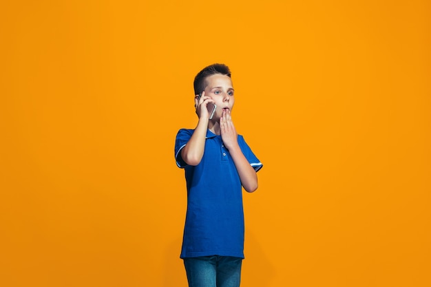 Foto gratuita el muchacho adolescente feliz de pie y sonriendo sobre fondo naranja.