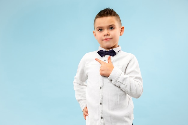 Muchacho adolescente feliz sonriendo aislado sobre fondo azul de estudio. Hermoso retrato masculino de medio cuerpo. Niño emocional joven apuntando a la izquierda. los