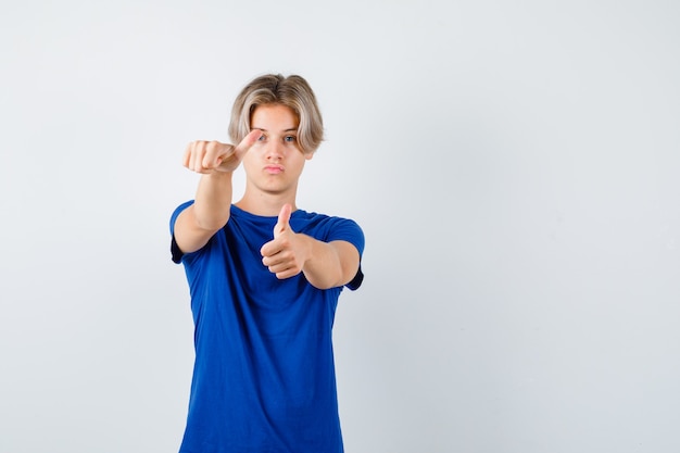 Muchacho adolescente hermoso que muestra los pulgares dobles para arriba en la camiseta azul y que parece confiado. vista frontal.