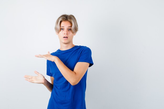 Muchacho adolescente hermoso que muestra el signo del tamaño en la camiseta azul y que parece desconcertado. vista frontal. Foto gratis