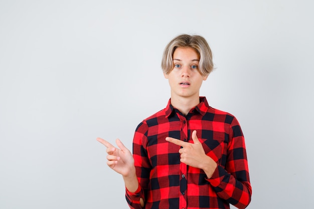 Foto gratuita muchacho adolescente joven apuntando hacia la izquierda en camisa a cuadros y mirando perplejo, vista frontal.