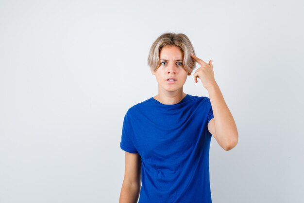 Muchacho adolescente joven apuntando a su cabeza en camiseta azul y mirando nervioso. vista frontal.