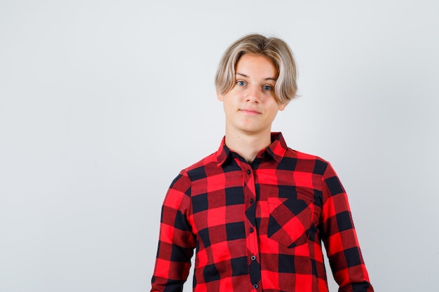 Foto gratuita muchacho adolescente joven en camisa a cuadros posando mientras está de pie y mirando confiado, vista frontal.