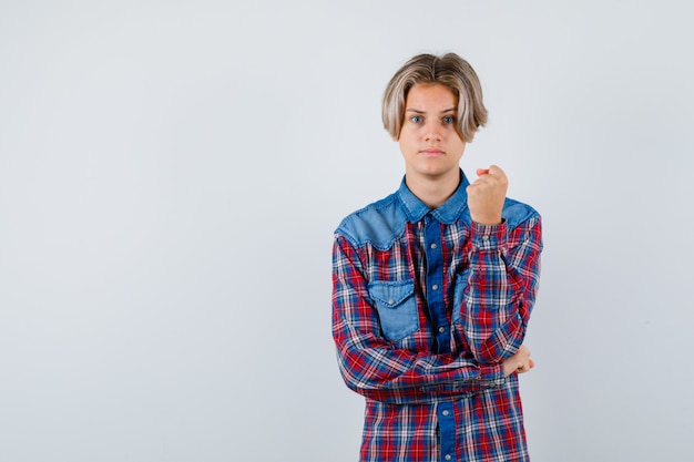 Muchacho adolescente joven en camisa a cuadros que muestra el puño cerrado y que mira seria, vista frontal.