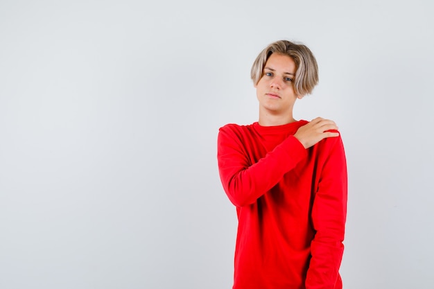 Muchacho adolescente joven con la mano en el hombro en suéter rojo y con aspecto cansado. vista frontal.